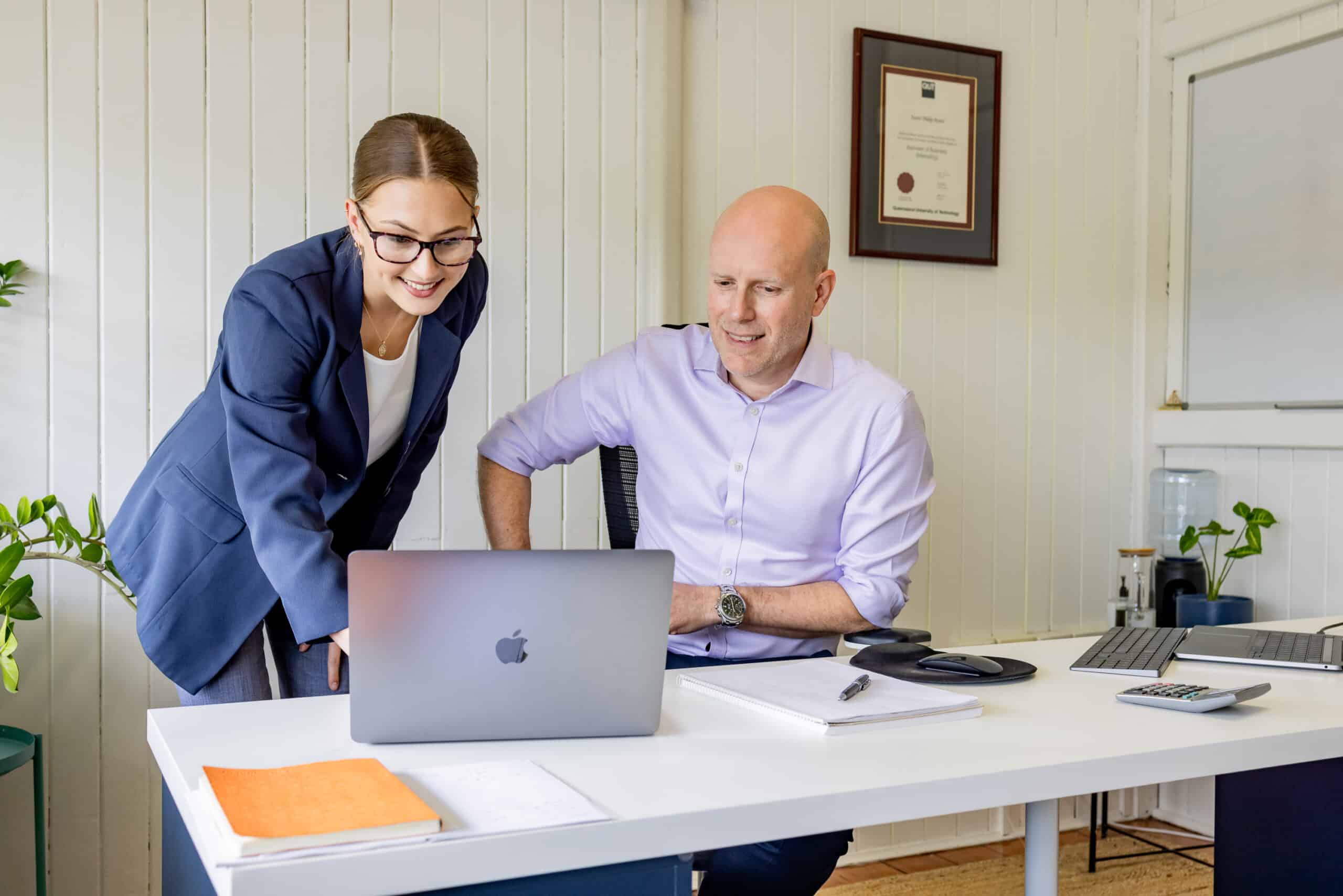 A female financial advisor and a male financial advisor are looking at a laptop screen as the female financial advisor shows the male something.