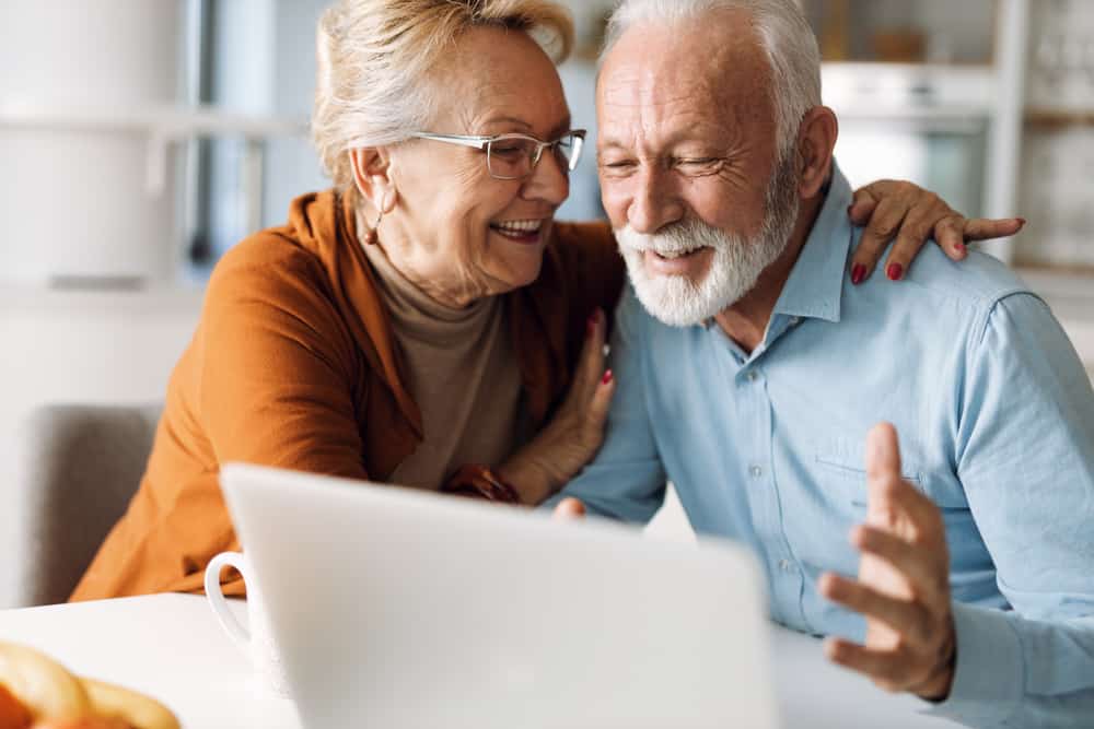 A mature couple smiling and using a laptop at their home.